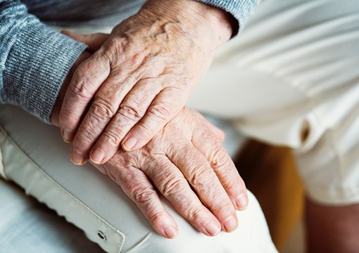 Ældre person sidder med hænderne foldet over hinanden.